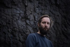 François J. Bonnet. Ein bärtiger Mann im blauen Pullover vor einer Mauer aus brüchigem Stein. Foto: Éléanore Huisse