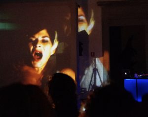 Szenenfoto aus XANTO, Ninfa in lamento. Zwei Leinwände hintereinander, darauf das Gesicht der Sängerin Sabina Meyer mit singend geöffnetem Mund. © Folkert Uhde